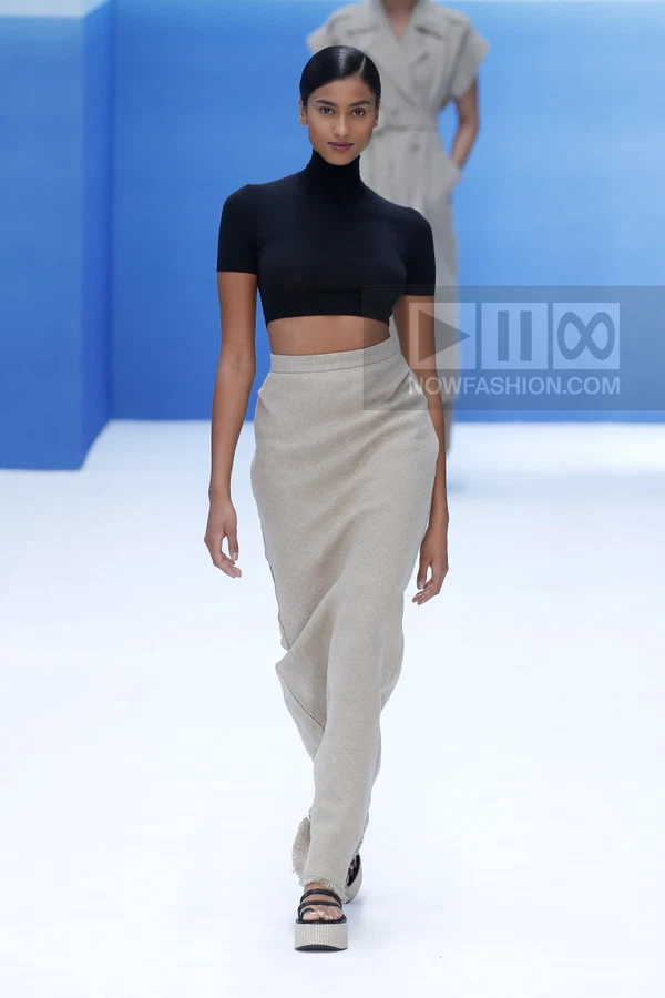A model walks the runway wearing a black cropped turtleneck top and a long beige skirt with raw hem details.