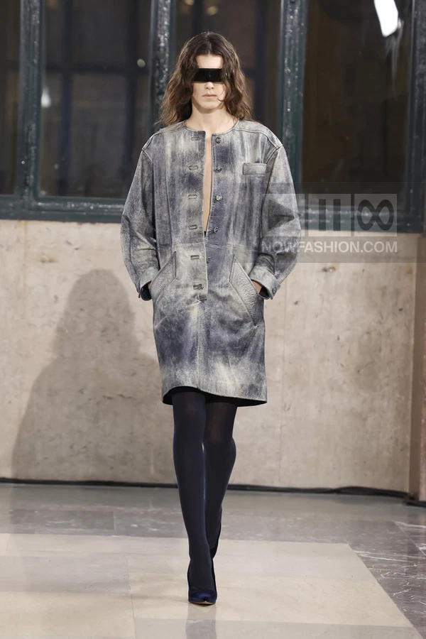 Model wearing a distressed gray leather coat with a buttoned front and dark tights on a runway.
