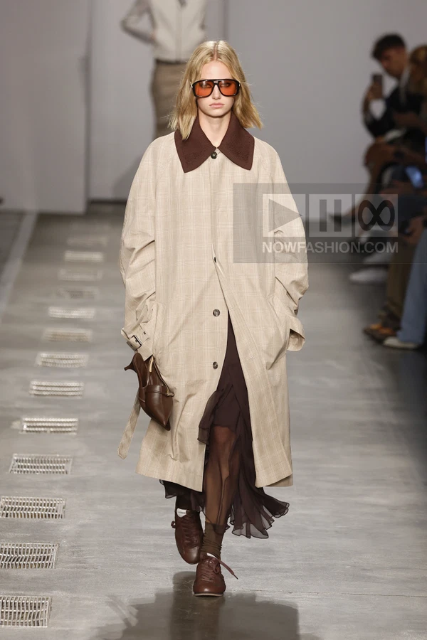 Model walking in a beige plaid trench coat over a dark brown sheer ruffled midi dress with brown sneakers and sunglasses.