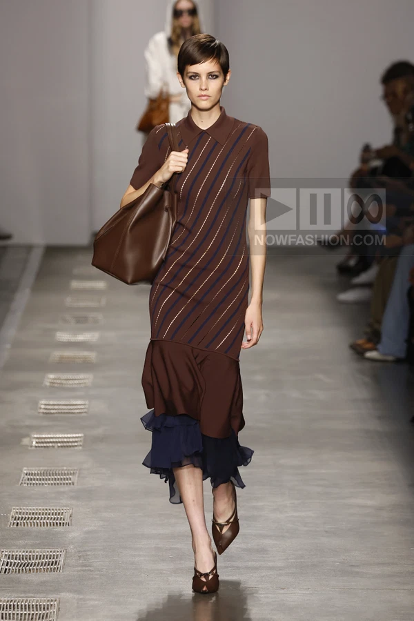 A model walks the runway wearing a brown polo-collar midi dress with diagonal stripes and a navy ruffled hem.