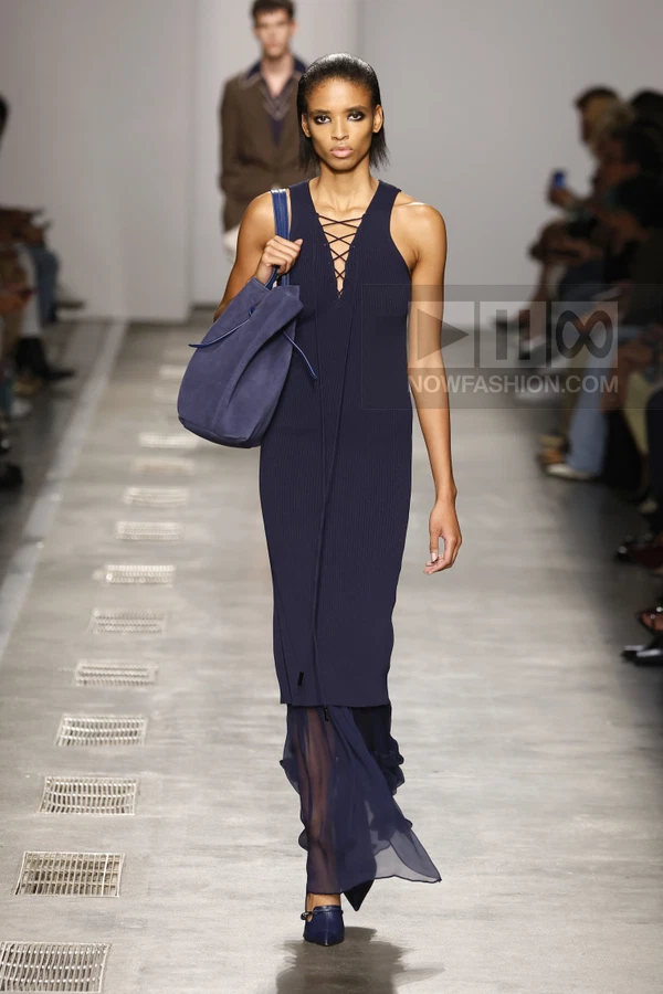 A model walks the runway in a navy blue ribbed midi dress with a lace-up neckline and a sheer chiffon hem.