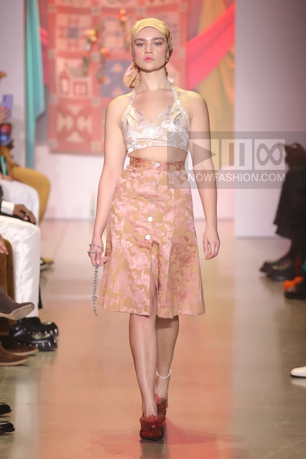 Model walking in a floral jacquard crop top and matching button-front midi skirt with a headscarf on a runway.