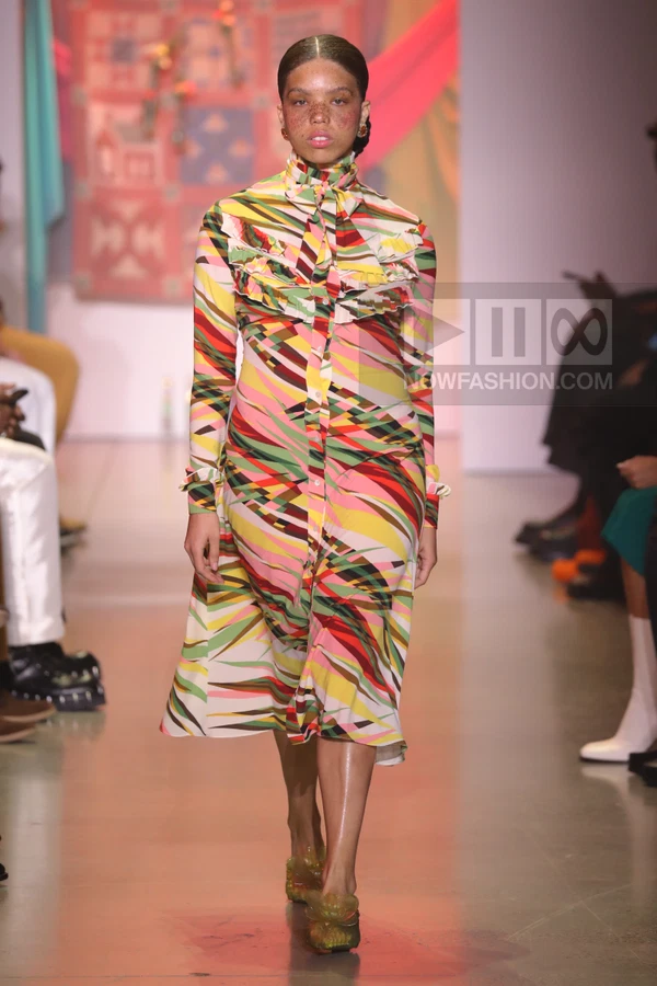 Model walking on runway wearing a long-sleeved midi dress with a colorful abstract geometric print and ruffled bodice.