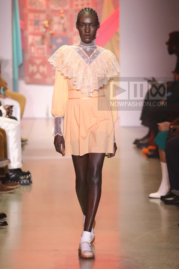 A model walks the runway in a peach-colored mini dress with a large lace collar and sheer high-neck yoke.