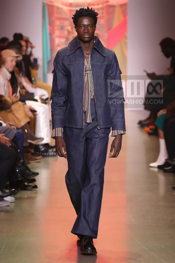 A model walks the runway in a dark wash denim jacket and matching wide-leg trousers over a striped shirt.
