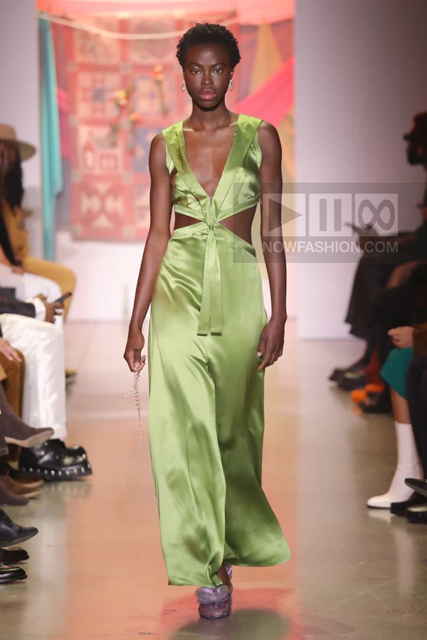 Model walking in a lime green satin maxi dress with waist cut-outs and a deep v-neckline on a runway.