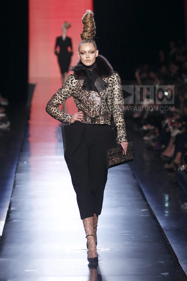 Model walking in a leopard print sequined biker jacket, black structured trousers, and leopard print tights on a runway.