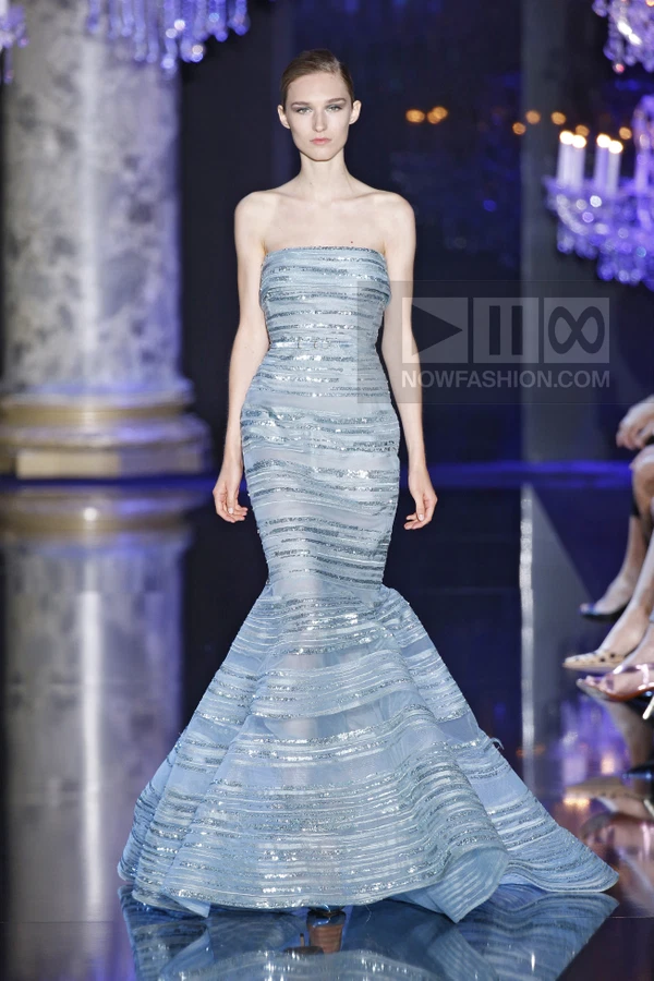 A model walks the runway in a strapless, floor-length light blue gown with horizontal silver sequin stripes.