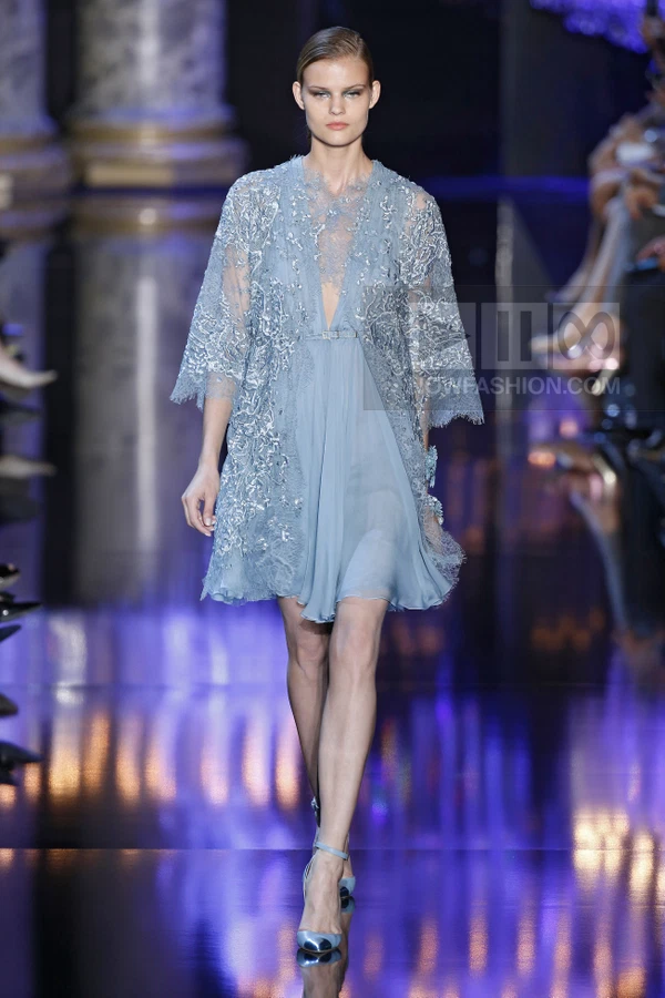 A model walks the runway in a light blue lace-embellished mini dress with sheer sleeves and matching heels.
