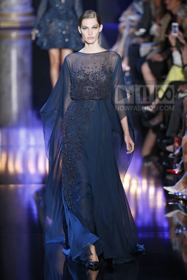 Model walking in a navy blue floor-length chiffon gown with beaded embellishments on the bodice and side panel.