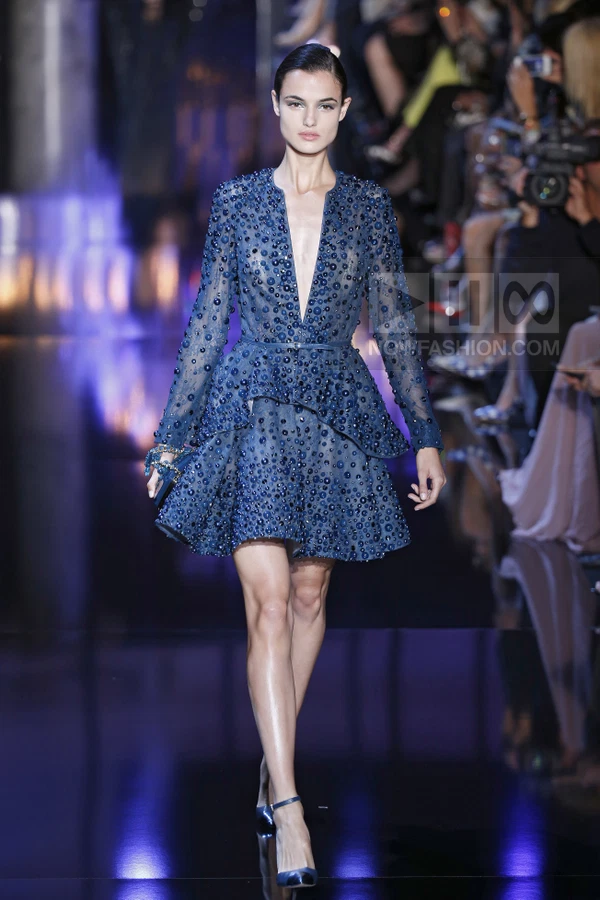 A model walks the runway in a blue long-sleeve mini dress with a peplum waist, embellished with beads and sequins.