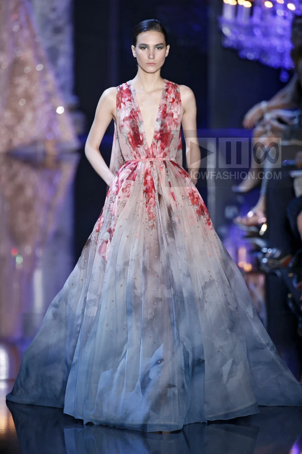 Model on runway wearing a floor-length sleeveless gown with a deep V-neckline, featuring a floral print and ombre effect.