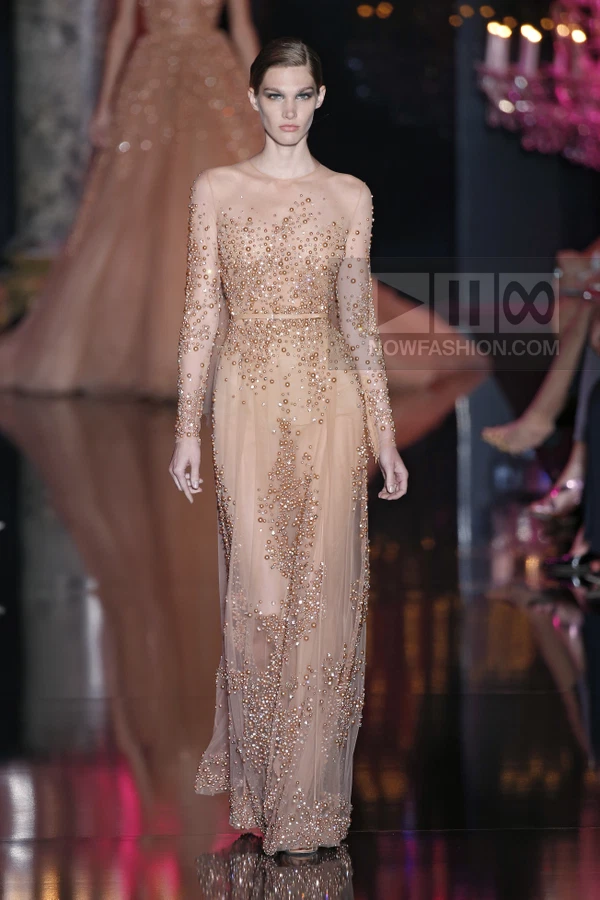 Model wearing a floor-length nude tulle gown with all-over pearl and bead embellishments on the runway.