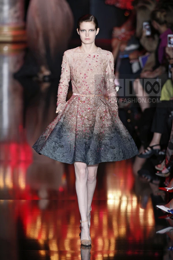 A model walks the runway in a long-sleeve mini dress with a gradient transition from beige to charcoal gray.
