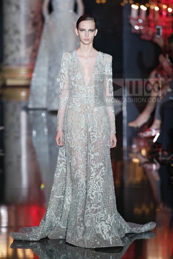 A model wearing a floor-length, sheer, light-blue gown with intricate embroidery and beading on a runway.