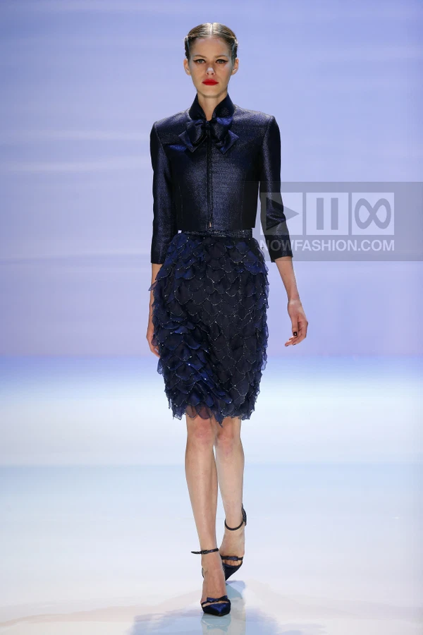 Model walking in a dark blue cropped jacket and a skirt covered in layered, petal-like fabric appliqués.