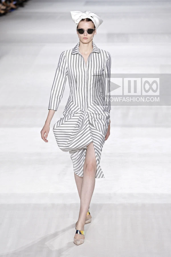 Model walking in a white and black striped midi dress with a draped hip detail, white headscarf, and metallic pumps.