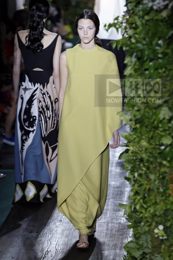 Model wearing a chartreuse sleeveless floor-length dress with an asymmetrical draped front panel on a runway.