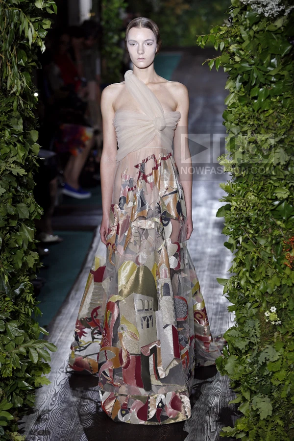 Model wearing a floor-length tulle gown with a nude bodice and a skirt featuring colorful architectural appliqué motifs.