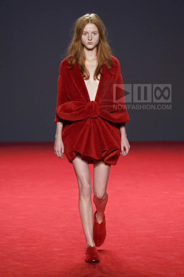 A model walks the runway in a red mini dress with a large bow detail at the waist and matching red shoes.