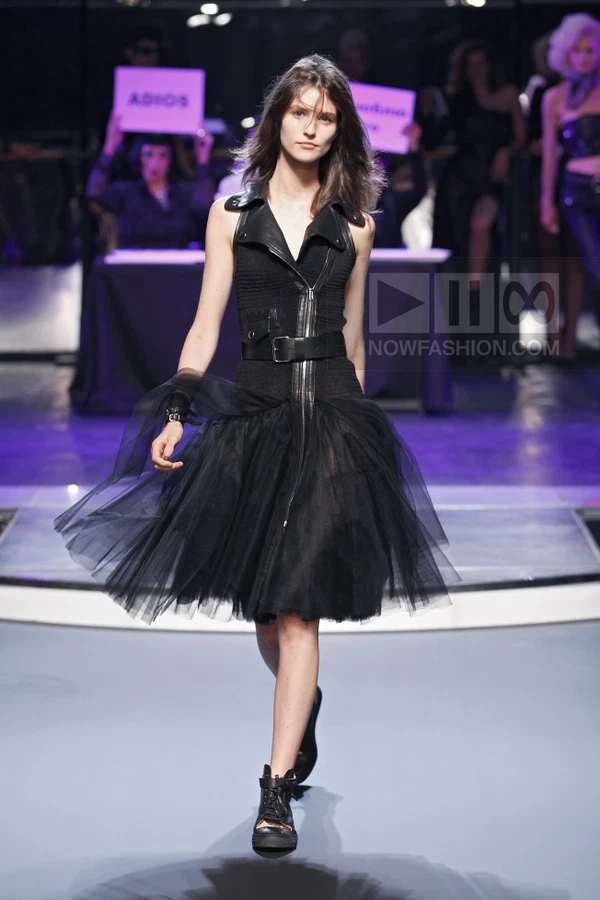 Model walking in a black sleeveless biker-style dress with a tulle skirt and black lace-up ankle boots on a runway.