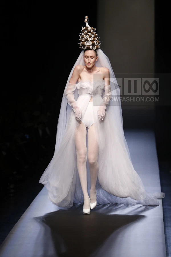 Model on runway wearing a white strapless bodysuit with tulle overlay, long gloves, and a hair-roller headpiece with veil.