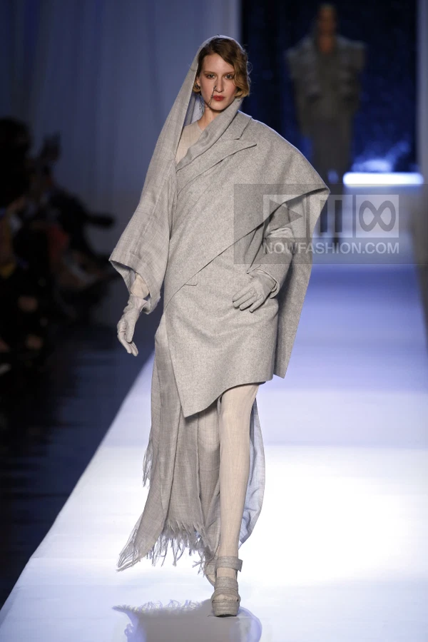 Model on runway wearing a gray wool coat with an integrated headscarf, matching gloves, and platform sandals.