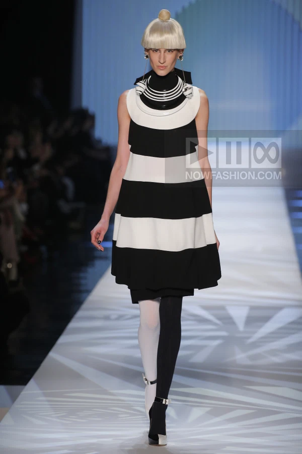 Model on runway wearing a black and white striped sleeveless mini dress with a high collar and color-blocked tights.