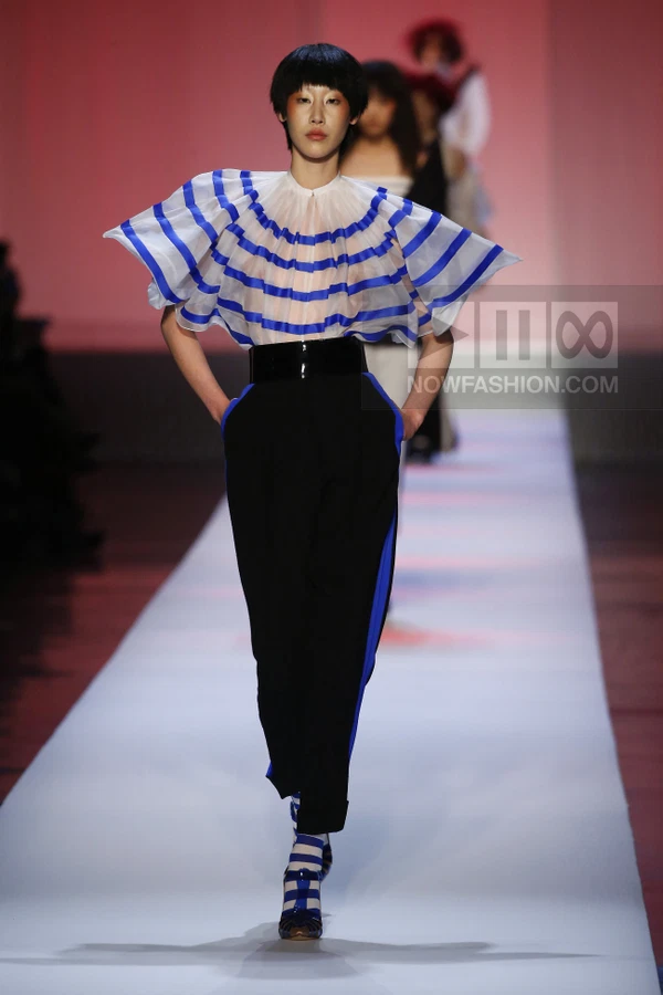 Model on runway wearing a white and blue striped ruffled top, black high-waist trousers, and matching striped socks.