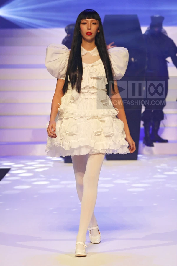 A model walks the runway in a white tiered mini dress with puffed sleeves and white tights.