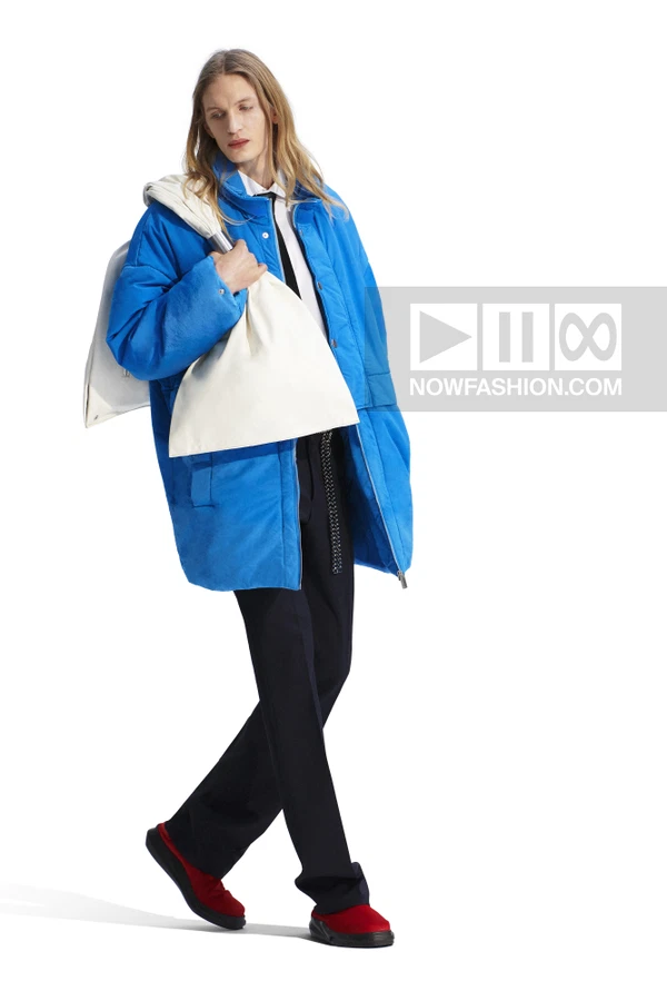 A person wearing a bright blue puffer jacket, white shirt, black tie, black trousers, and red slip-on shoes.