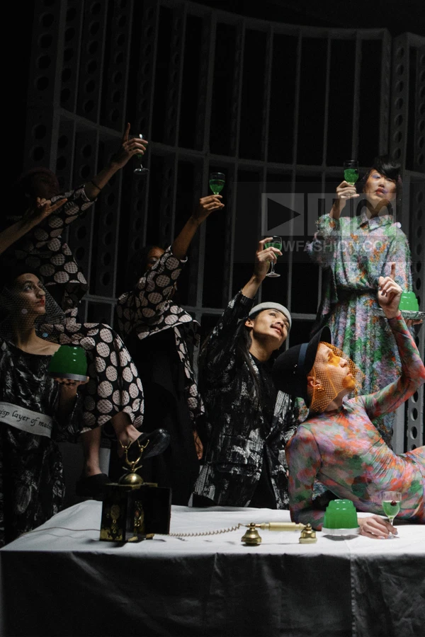 Group of people in patterned garments posing around a table with green gelatin and a vintage telephone.