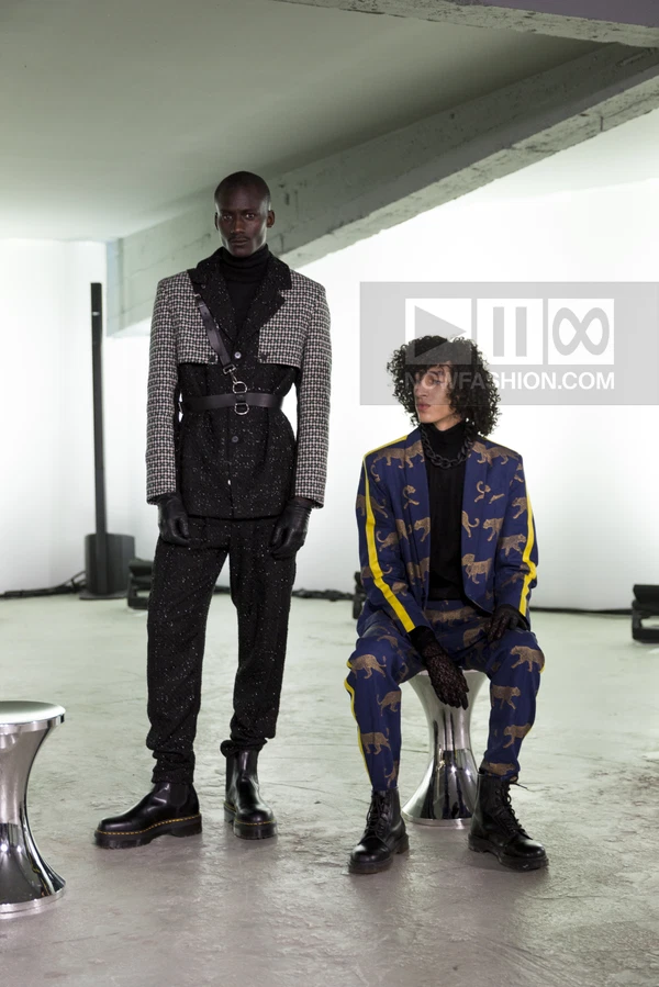 Two models in a studio; one standing in a black tweed suit with houndstooth shoulders, one seated in a blue leopard suit.
