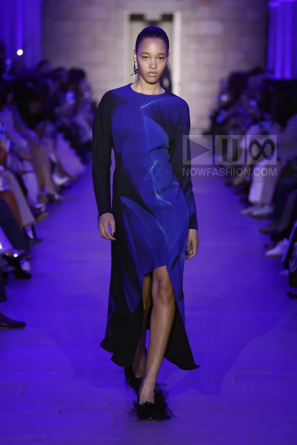 Model walking the runway in a long-sleeved blue and black abstract print midi dress with an asymmetric hem.