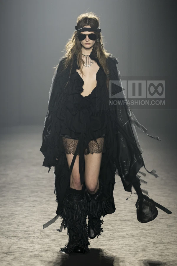 Model wearing a black ruffled blouse, lace shorts, and fringed boots on a runway.