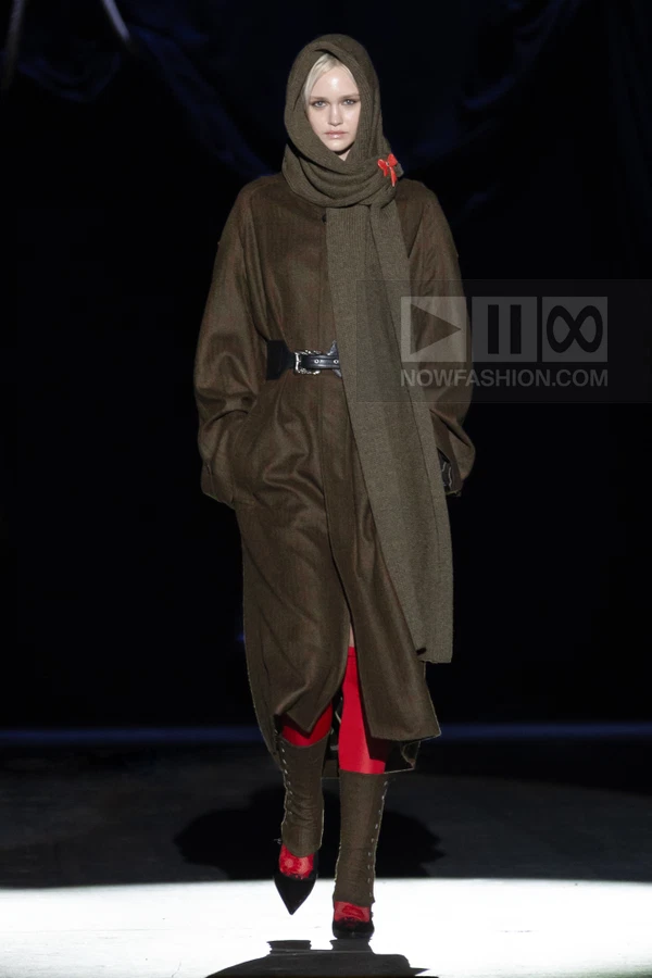 Model wearing a long brown wool coat, matching headscarf, black buckled belt, and red tights with lace-up boots.