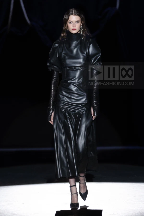 A person walks on a runway wearing a black leather midi dress with puff sleeves and a high collar.