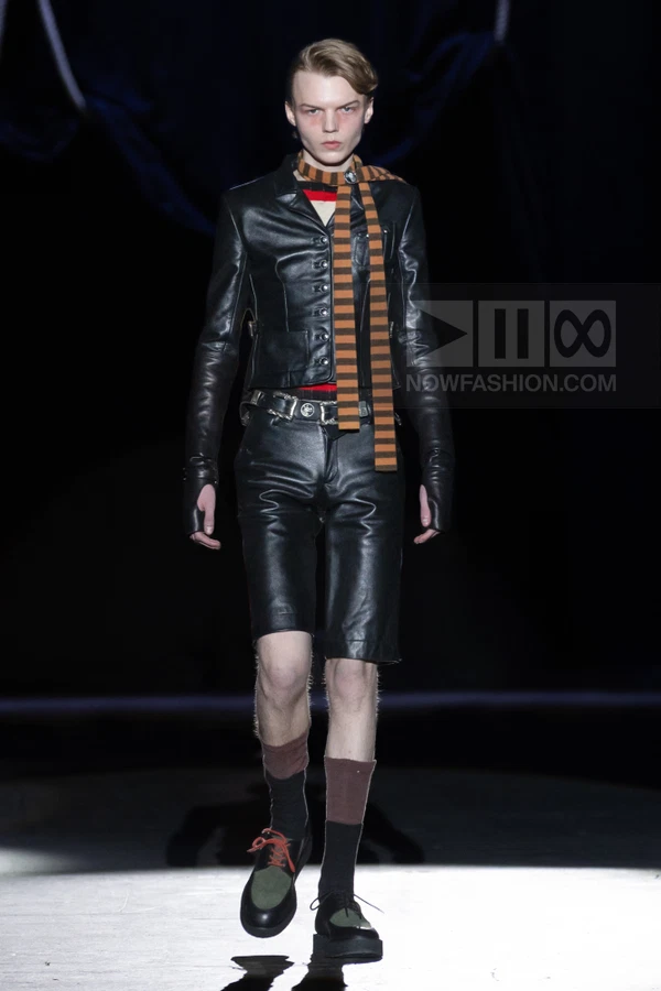 Model wearing a black leather jacket and matching leather shorts with a striped scarf on a dark runway.