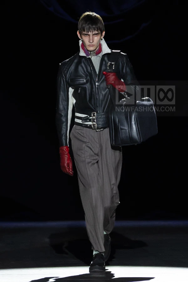 Model walking in a black leather biker jacket, gray pinstripe trousers, red leather gloves, and a large black holdall bag.