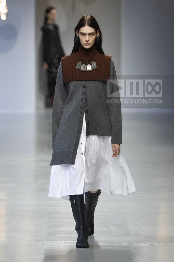 Model walking in a gray cardigan, brown ribbed collar, white shirt dress, and black knee-high boots on a runway.