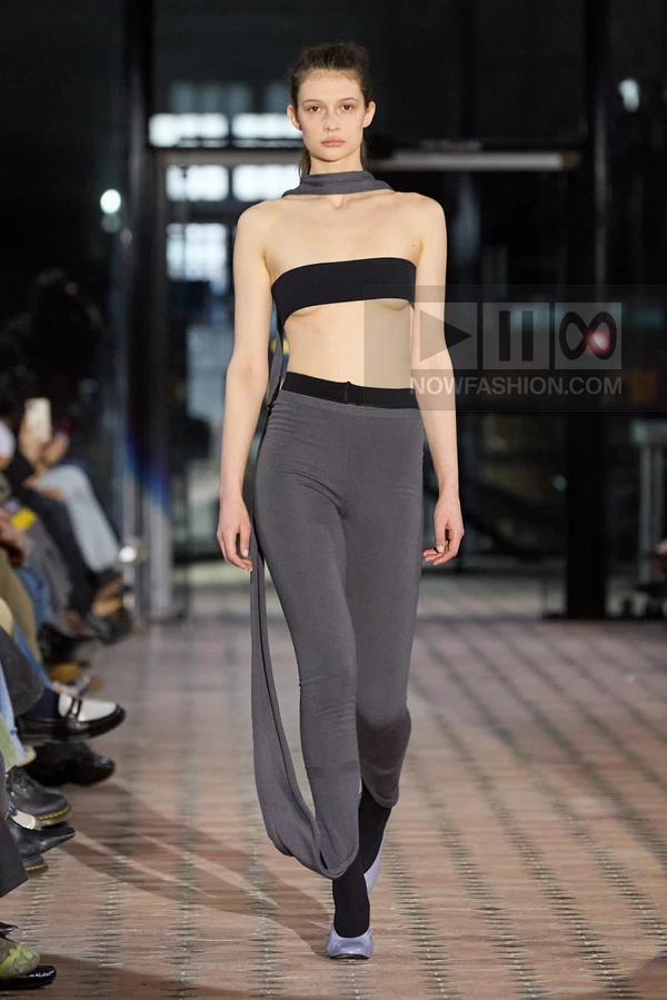 A model walks the runway in a charcoal gray bandeau top and matching leggings with a long scarf-like neck tie.