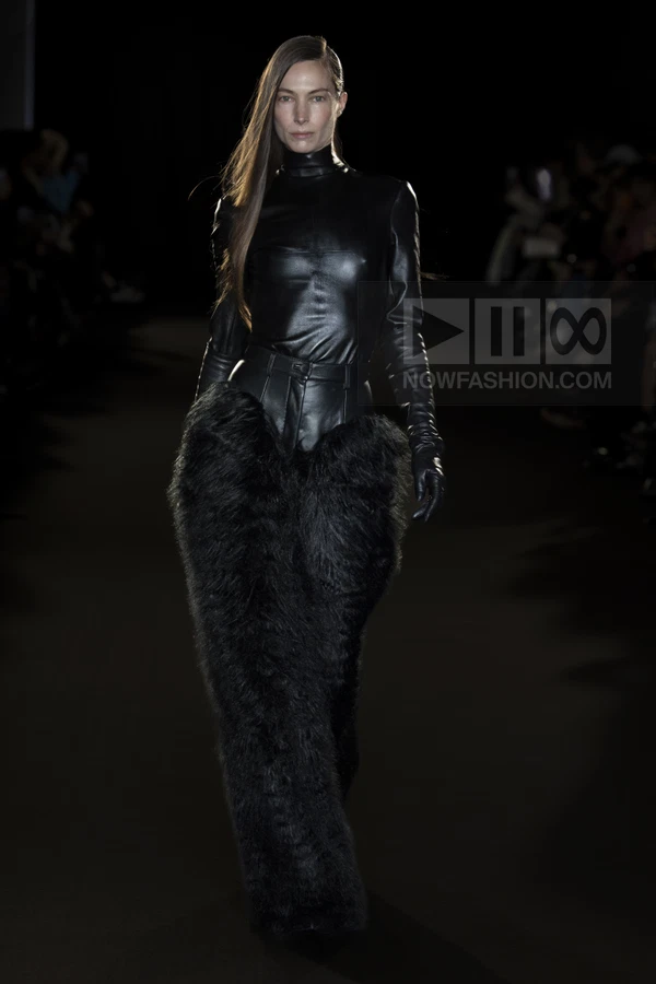 A model walks the runway in a black leather long-sleeve top and matching leather pants with large black fur side panels.