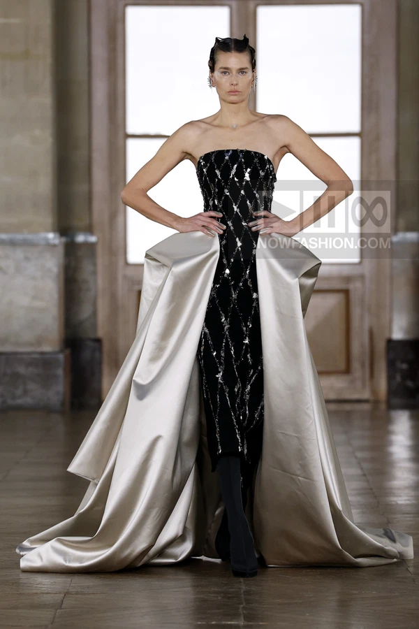 Model wearing a black strapless gown with silver diamond-patterned embellishments and a voluminous cream overskirt.