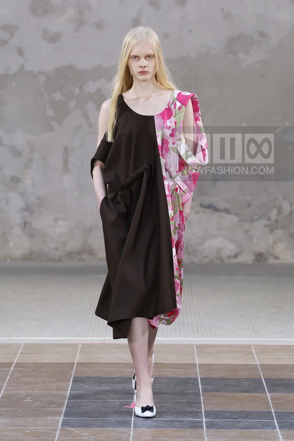 A model walks the runway in a two-tone midi dress featuring a solid brown side and a floral pink side.
