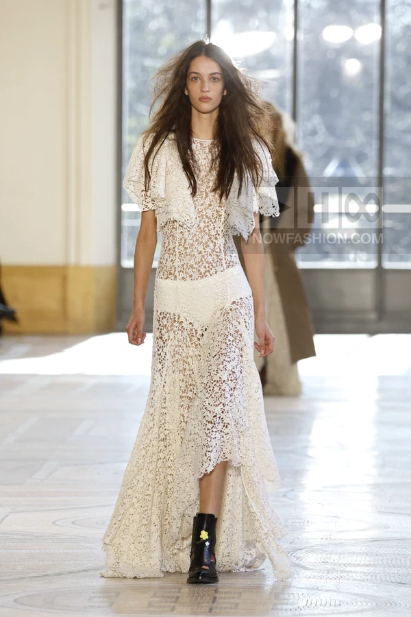 A model walks the runway in a white lace midi dress with flutter sleeves, paired with black leather ankle boots.