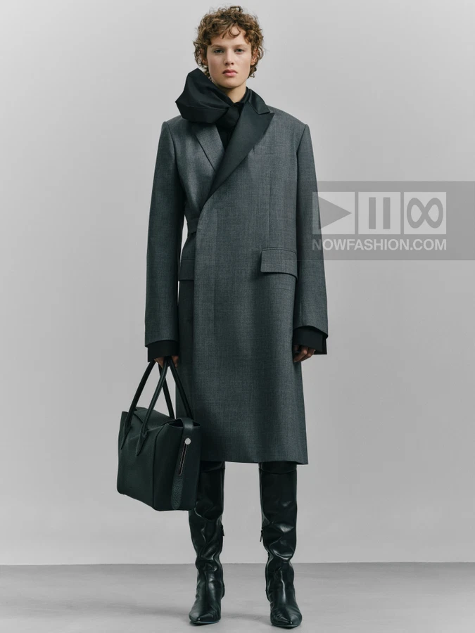 A person wearing a gray wool coat with black lapels, a black scarf, and black leather boots, holding a black tote bag.